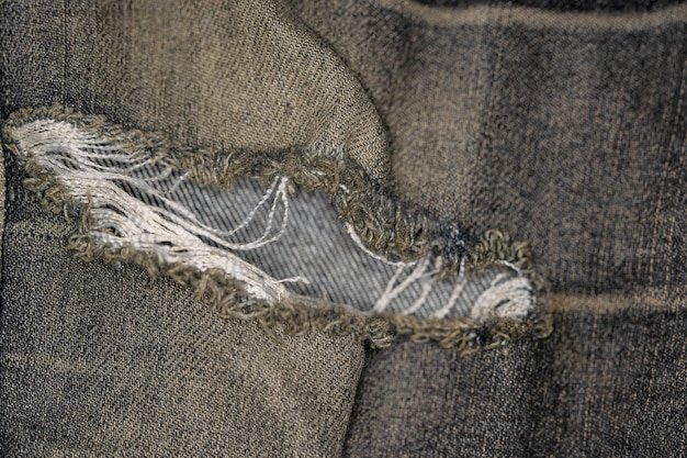 A close-up photograph showing the worn and frayed fabric of a pair of trousers, with visible stress points around seams and pockets. The fabric has a faded appearance, suggesting repeated wear and washing.